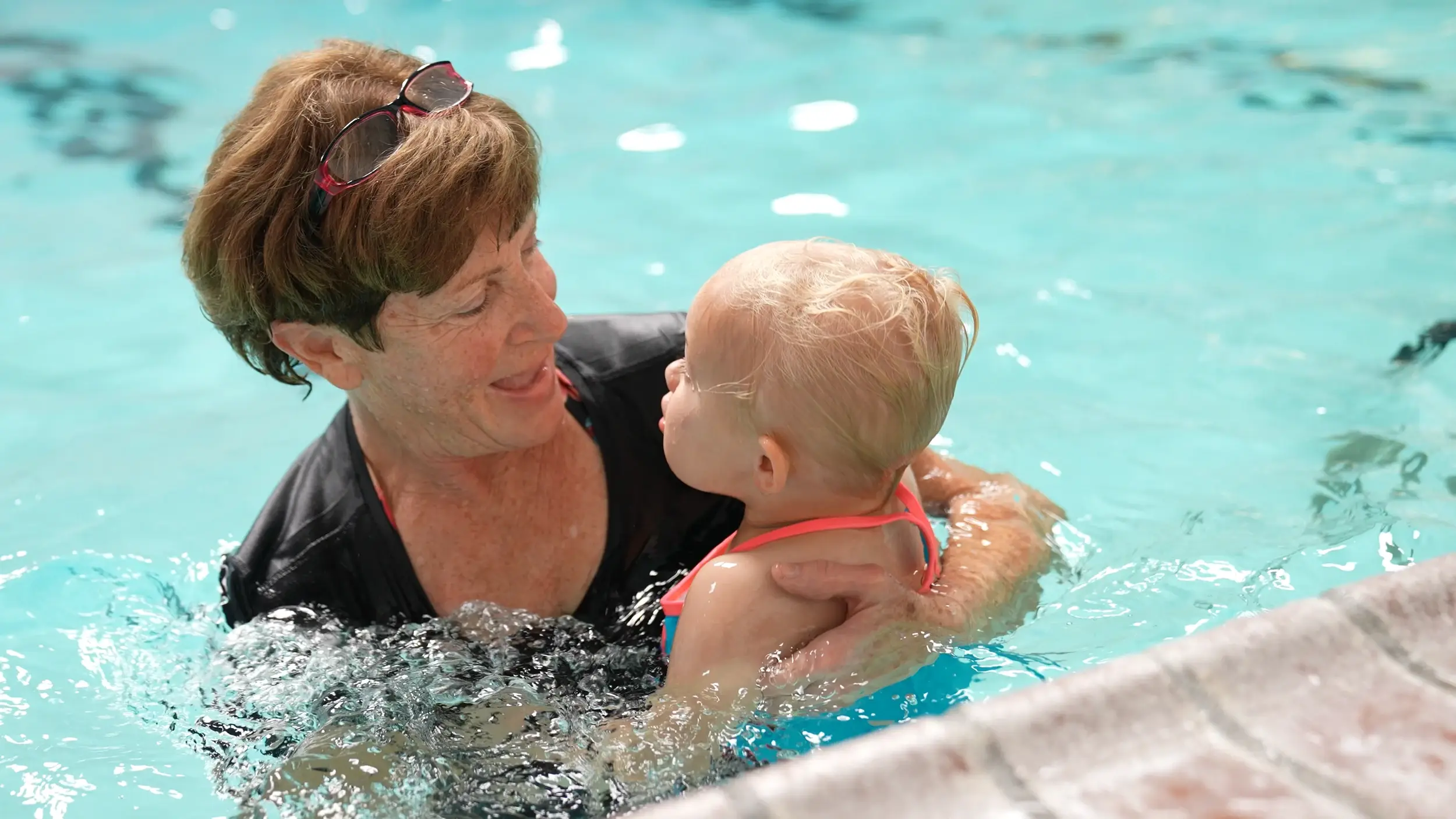 An instructor holds a toddler securely during an infant swim lesson