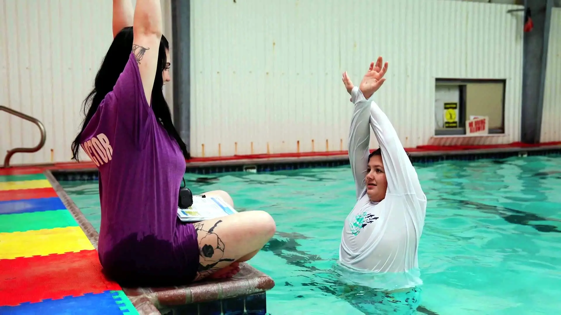 An instructor stretches beside a swimmer in the pool