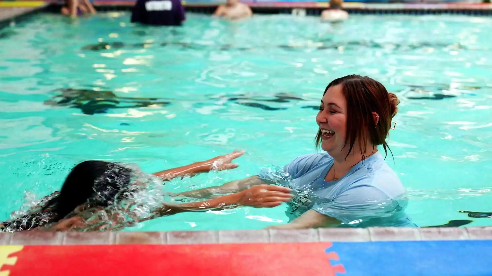 An instructor welcomes a child swimming toward them